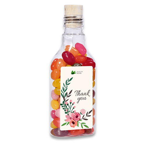 Įvairių vaisių skonių želė saldainiai „Jelly beans“ mažame stikliniame buteliuke su reklamine etikete. 